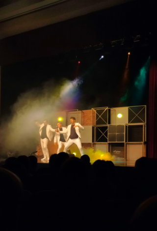 na scenie trzech mężczyzn w rozpiętych garniturach na zadymionej scenografii